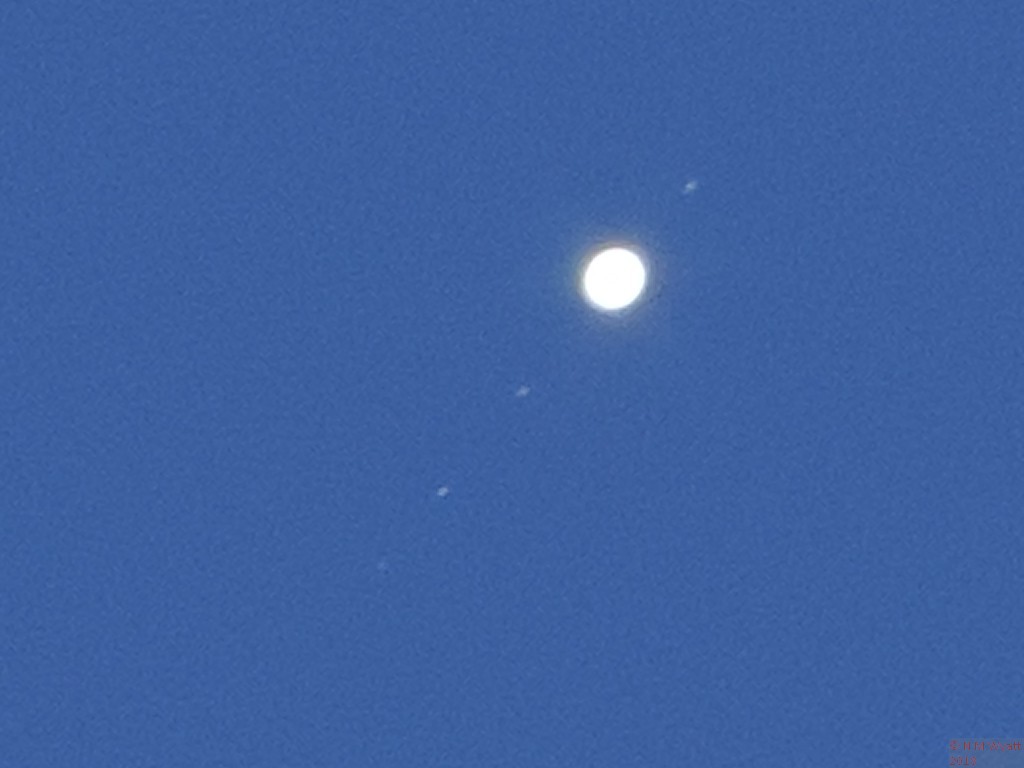 Jupiter and four moons in a blue sky